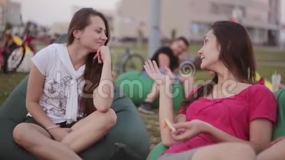 两个美丽的黑发女孩姐妹在公园里聊天夏天坐在豆袋椅子上视频的预览图