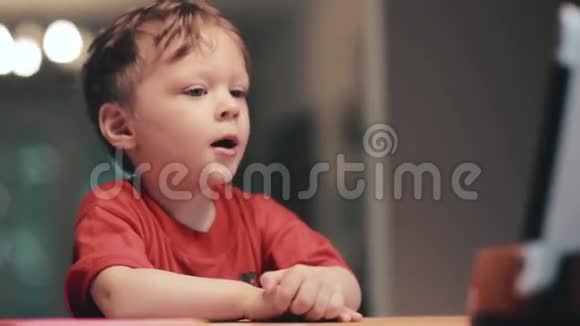 穿红色衬衫的小男孩坐在平板电脑前打哈欠视频的预览图