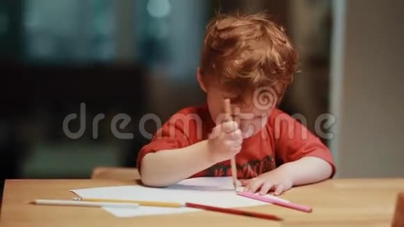 一个可爱的小男孩坐在桌子旁用白纸上的彩色铅笔画画视频的预览图
