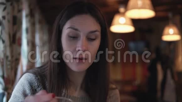年轻迷人的黑发女人坐在咖啡馆里用勺子说话和吃饭一个女孩在和别人谈话视频的预览图