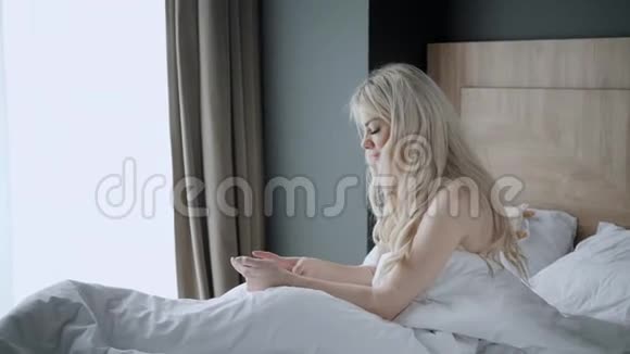 用电话检查电子邮件和社交媒体信息少妇醒来坐在舒适的床上上午酒店视频的预览图
