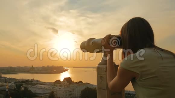年轻女子透过观光望远镜在日落时分探索城市视频的预览图