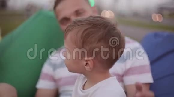 快乐的爸爸亲吻他可爱的儿子的脸颊父亲和儿子夏天在公园里消磨时间男孩指着什么视频的预览图
