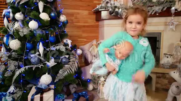 小女孩和一个娃娃一起跳舞小圆头在圣诞树附近庆祝新年除夕一个快乐的小女孩视频的预览图