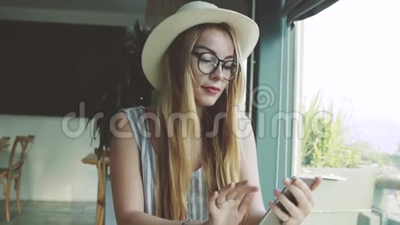 在咖啡馆的智能手机上看照片的女人年轻女孩喝着咖啡微笑着视频的预览图