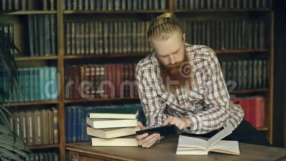 在图书馆里读一本书用平板电脑准备考试的小胡子学生视频的预览图