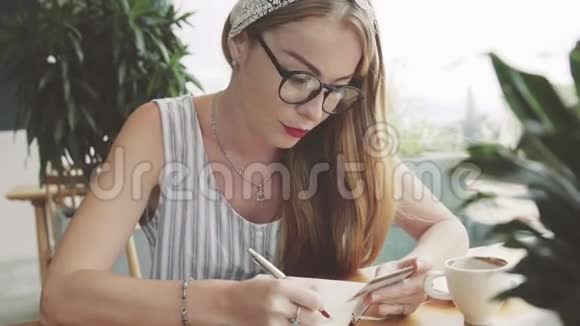 年轻漂亮的女人从卡片到笔记本都在写信息女作家在咖啡馆写作视频的预览图