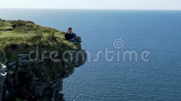 坐在爱尔兰西海岸悬崖边上的年轻女子视频的预览图