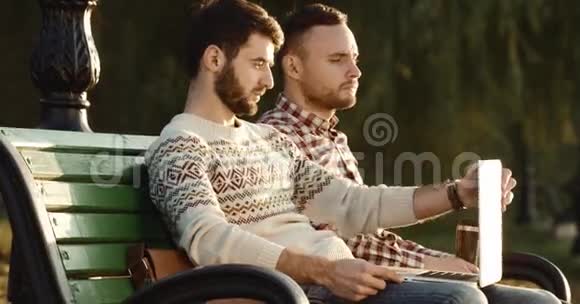 两个人坐在长凳上打开笔记本电脑聊天写4k视频的预览图