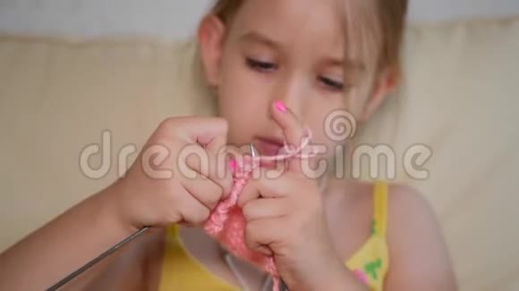 小女孩坐在沙发上编织羊毛围巾小女孩在家里用针编羊毛衣服视频的预览图