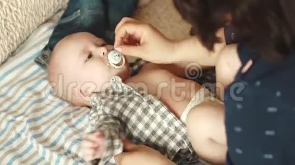 妈妈给她的小儿子穿上衬衫妈妈照顾孩子婴儿嘴里放着奶嘴视频的预览图