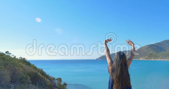 那个年轻的女孩在海上的山上举起了双手清澈的海水碧水视频的预览图