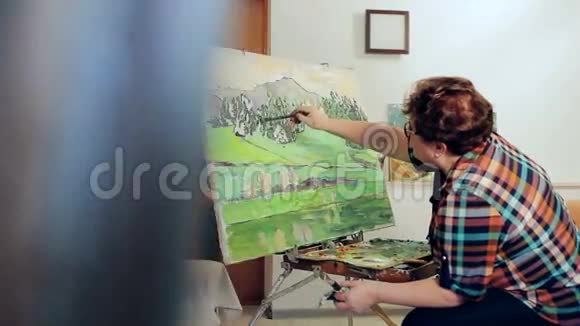 一个女人用调色板和画笔用油画颜料描绘风景投中弹视频的预览图