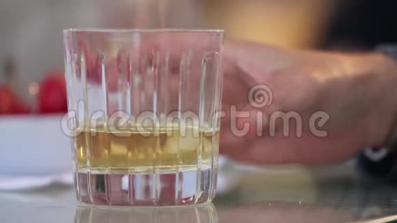 男人从桌子上拿出一杯加冰的威士忌把一杯加冰的威士忌放在桌子上特写视频的预览图