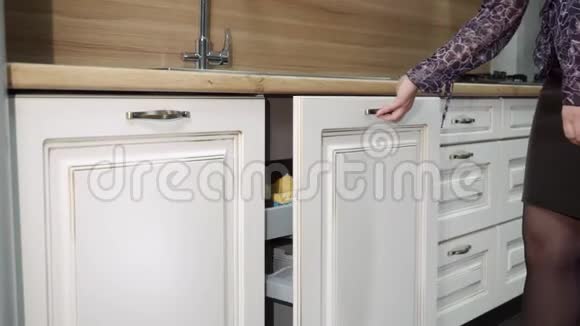 女孩打开水槽下面的抽屉展示着厨房橱柜的填充经典的厨房布景视频的预览图