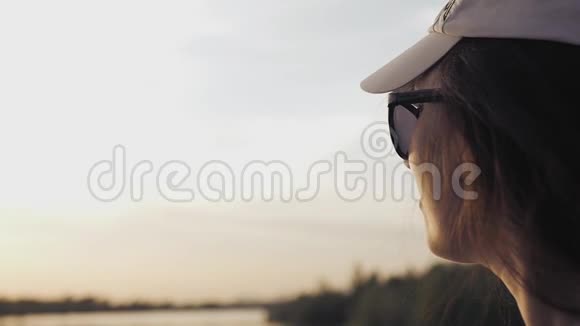 一个戴着帽子戴着眼镜的女孩欣赏湖面上的日落高清1920x1080视频的预览图