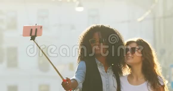 在阳光明媚的街道上散步时迷人的多民族女孩戴着太阳镜自拍的近景视频的预览图