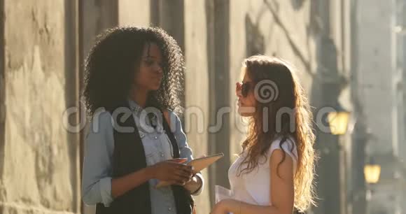 两个美丽的多元文化女朋友正在阳光明媚的街道上散步视频的预览图