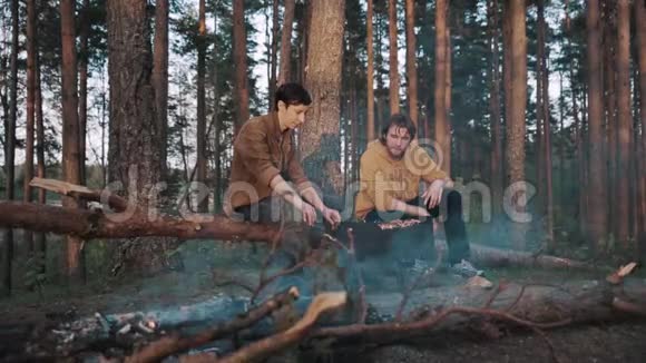 两个男朋友坐在森林里的原木上做烧烤聊天视频的预览图