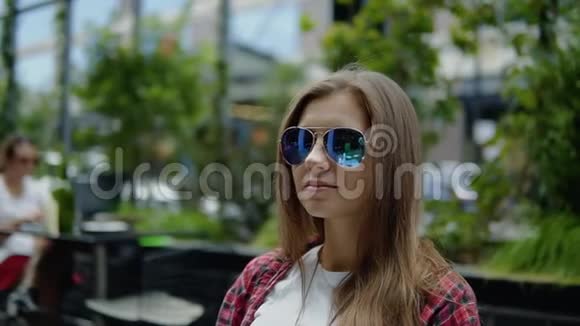 可爱的年轻女孩戴着时尚的眼镜在城市的咖啡馆里喝着新鲜的水视频的预览图