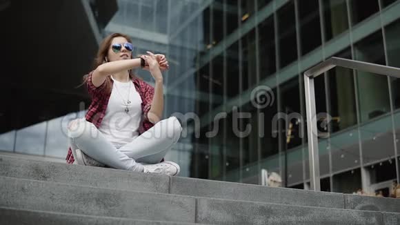 漂亮的年轻女子戴着眼镜穿着休闲服在台阶上看手表的时间视频的预览图