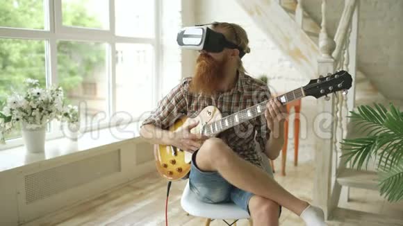 坐在椅子上学着用VR360耳机弹吉他在音乐会上感觉他是吉他手视频的预览图