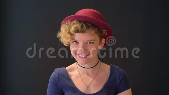 美丽的年轻女子头上戴着一头卷发戴着帽子对着镜头微笑站在黑色背景上与世隔绝视频的预览图