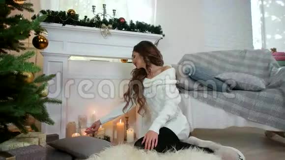 许愿手里拿着蜡烛的女孩坐在壁炉和圣诞树旁想着新年愿望视频的预览图