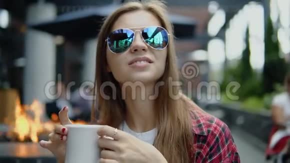 满意的年轻可爱的女孩坐在街头咖啡馆喝茶视频的预览图