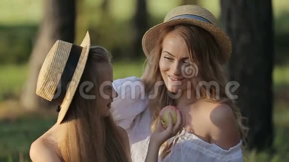 一位快乐的母亲和幸运的女儿在一个城市公园野餐时坐在一起玩苹果视频的预览图