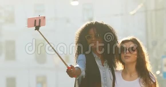 漂亮的带着太阳镜的微笑女朋友在街上散步时用自拍棒拍照视频的预览图