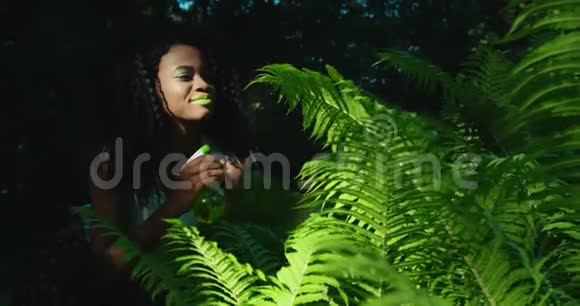 美国黑人女孩的敏感户外肖像用绿色的蕨类植物喷洒明亮的绿色化妆视频的预览图