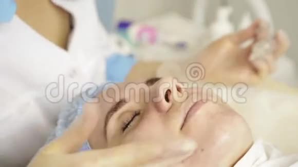 美丽的女人在水疗沙龙接受美容治疗美容医生戴着医用手套摸着女孩脸视频的预览图