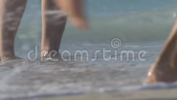 美丽的女性脚在海滩上行走腿被海水冲刷在沙滩上有很多脚波浪视频的预览图