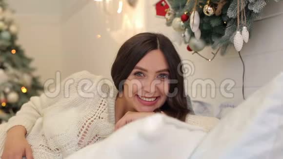 怀孕的女孩躺在圣诞树附近的床上视频的预览图