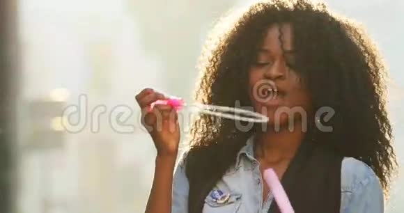 快乐的美国黑人女孩在阳光明媚的日子里一边吹肥皂泡一边玩视频的预览图