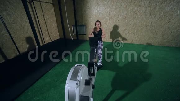 穿着灰色裤腿的漂亮金发女孩在健身房划船锻炼身体视频的预览图