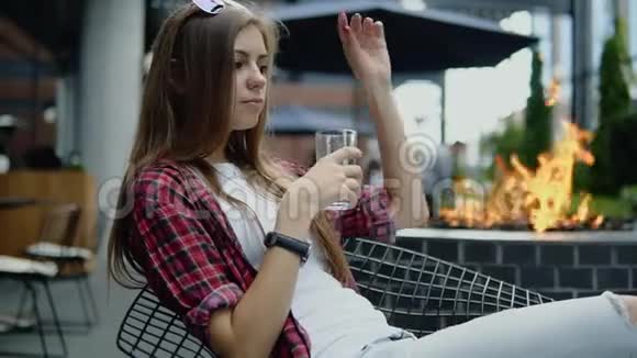 迷人的年轻女孩长着棕色头发穿着休闲服坐在城市街头的咖啡馆里喝着冷水视频的预览图