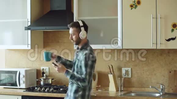 一个英俊的年轻人戴着耳机在家里的厨房里跳舞唱歌在假期里玩得开心视频的预览图