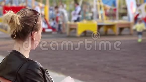 你的女人用手机坐在长凳公园里戴着时尚的酷墨镜妈妈等着她的女儿而她却在玩耍视频的预览图