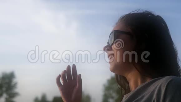 一个女孩戴着太阳镜站在蓝天上试图把它们摘下来慢动作1920x1080高清视频的预览图