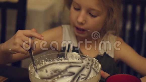 一个迷人的小女孩在做蛋糕后贪婪地吃厨房里剩下的奶油视频的预览图