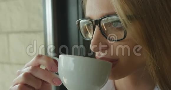 这位戴着眼镜的金发美女的特写肖像享受着这杯茶视频的预览图