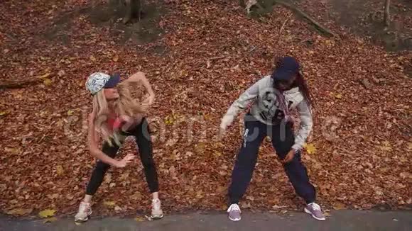横向看两个多元文化的女朋友拉下来在秋天的公园里弯着腰视频的预览图