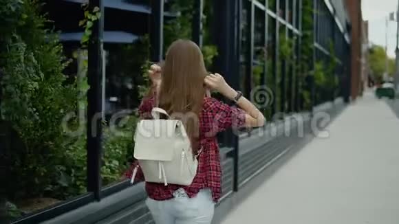 留着长发和背包的年轻女子在城市街咖啡厅附近散步视频的预览图