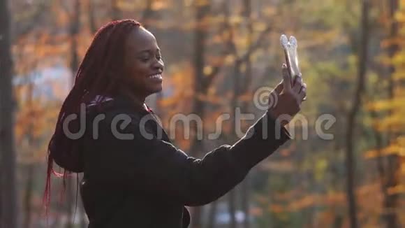秋天公园里一个快乐的美国黑人女孩在通过手机聊天时大笑的侧面肖像视频的预览图