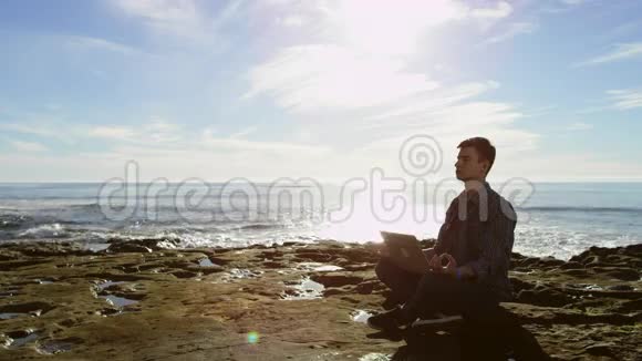 有魅力的年轻人拿着笔记本电脑坐在海边沉思视频的预览图