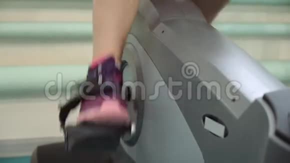 漂亮的女孩在健身房里骑着一辆静止的自行车锻炼女孩骑着运动自行车运动鞋特写视频的预览图