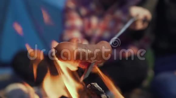 在篝火上烤香肠露营者烤香肠游客们正坐在火焰旁边视频的预览图