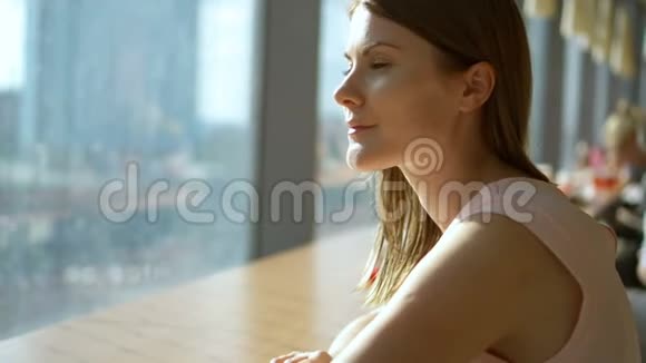 一幅美丽梦幻的年轻女子坐在靠近窗户的咖啡馆的桌子前思考的肖像美食广场视频的预览图